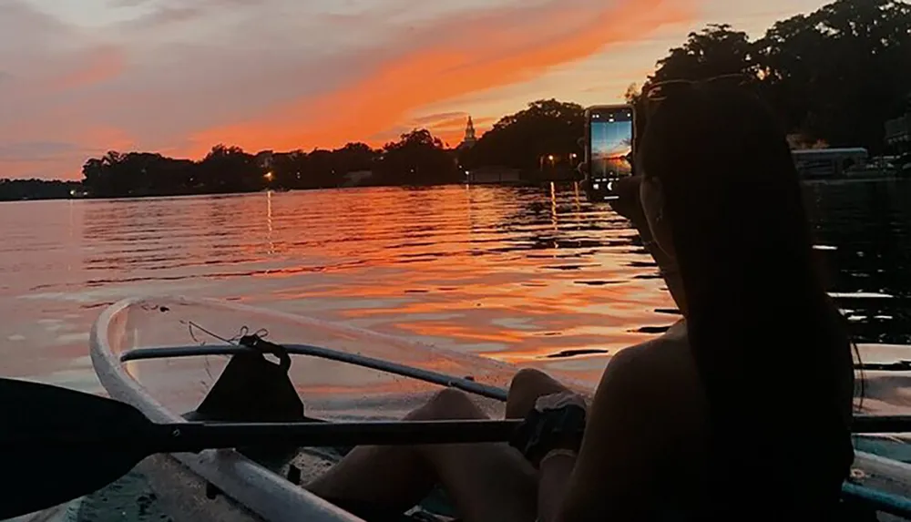 A person is kayaking on calm waters with a stunning sunset in the background