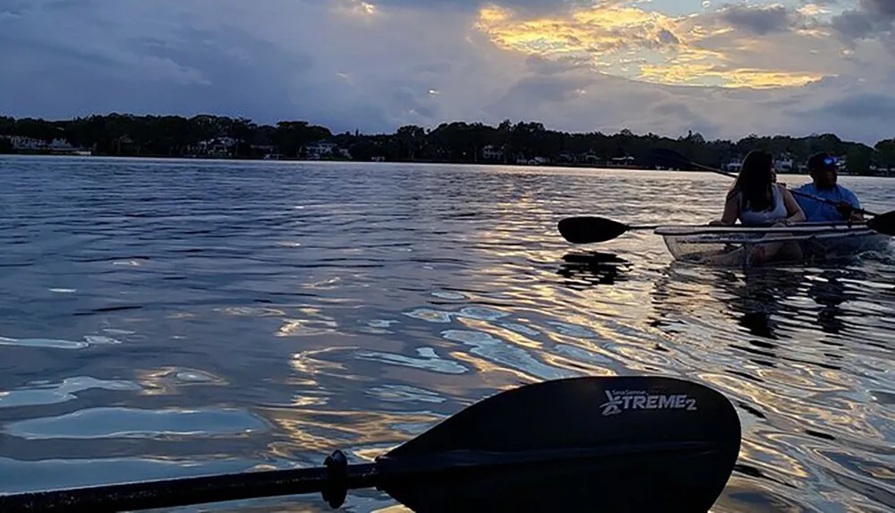 Two people are kayaking on a serene body of water during a striking sunset