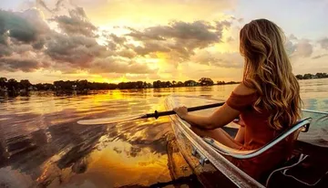 A person is kayaking on calm water during a vibrant sunset.