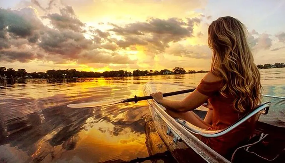 A person is kayaking on calm water during a vibrant sunset