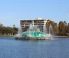 A waterfront view from a wooden deck featuring a city skyline and a fountain in the center of a lake under a blue sky