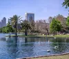 A waterfront view from a wooden deck featuring a city skyline and a fountain in the center of a lake under a blue sky