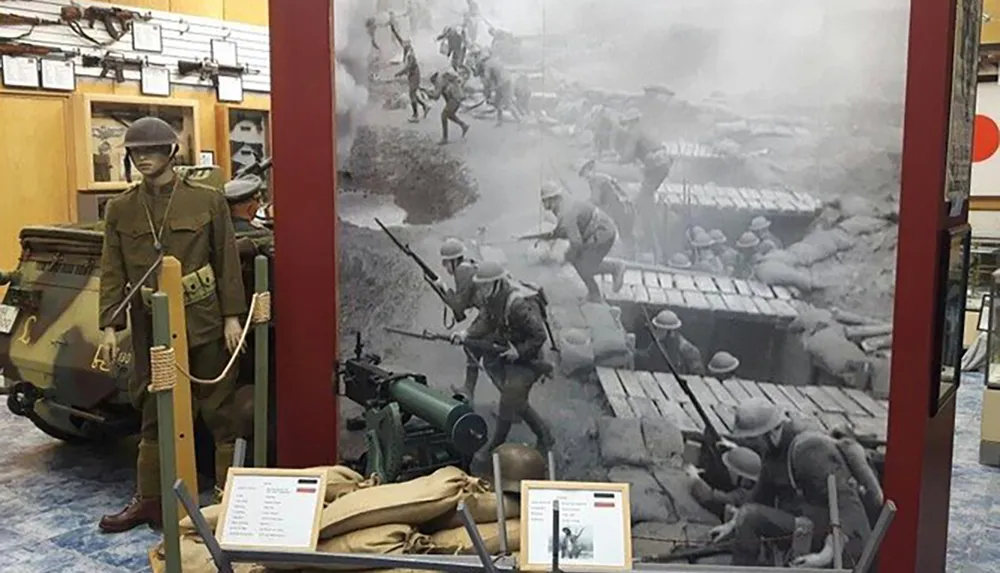 The image shows a museum display with a life-sized mannequin dressed in military attire a backdrop photo of a historic battle and various wartime artifacts and informational placards