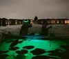 A person is kayaking at night in a clear kayak illuminated from within highlighting the water below