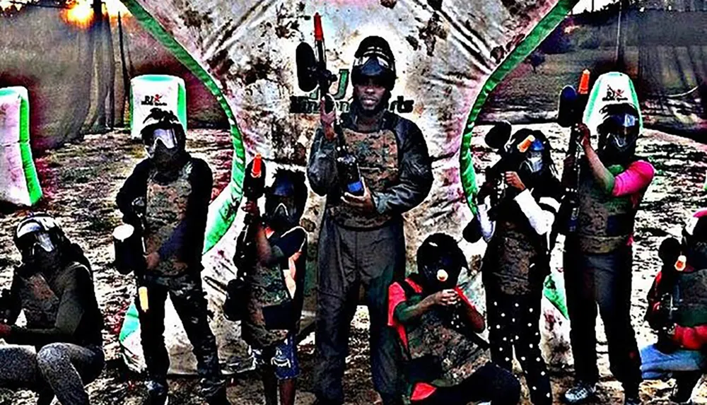 A group of people equipped with paintball gear and guns pose for a photo at a paintballing event