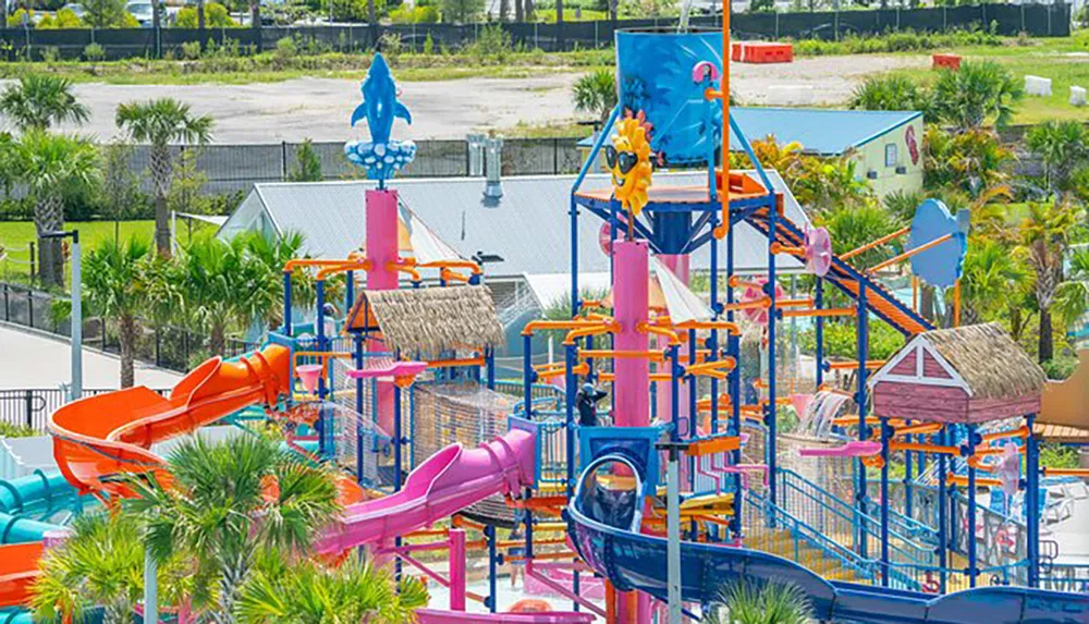 The image shows a colorful water park with slides water features and play structures set amidst palm trees and a sunny backdrop