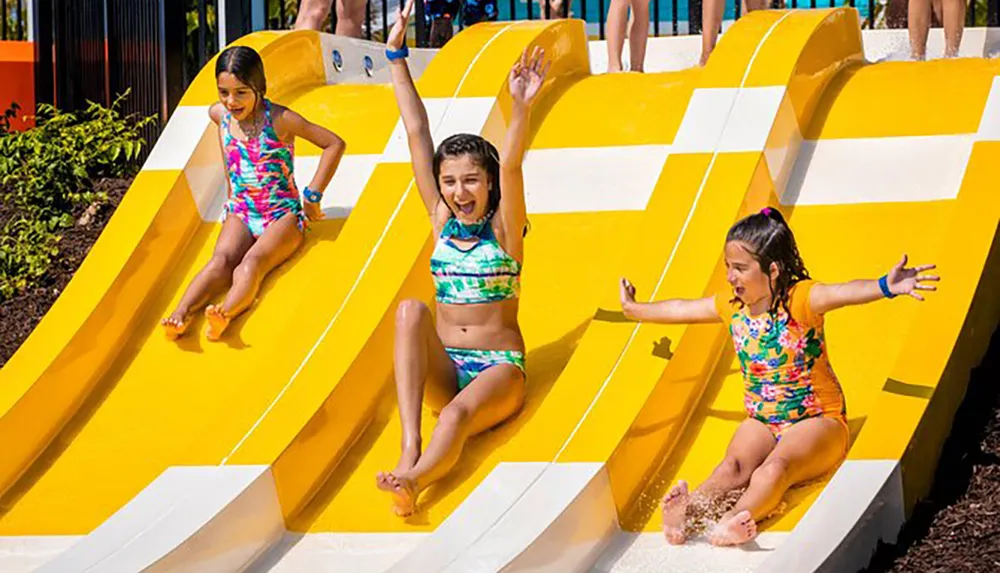 Three children are enjoying themselves as they slide down a bright yellow water slide at an amusement park