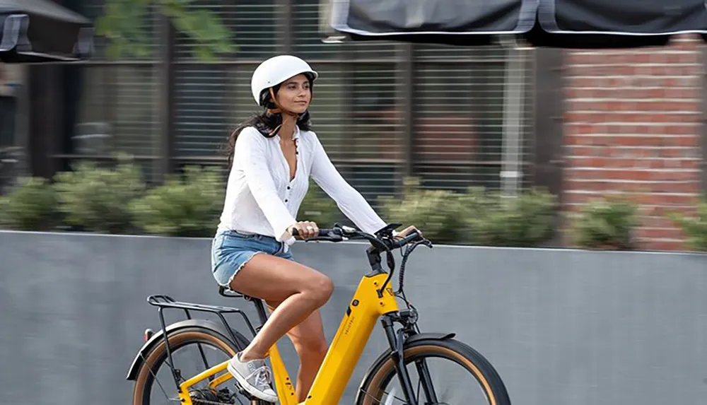A person wearing a white helmet and casual clothing is riding a yellow bike on an urban street