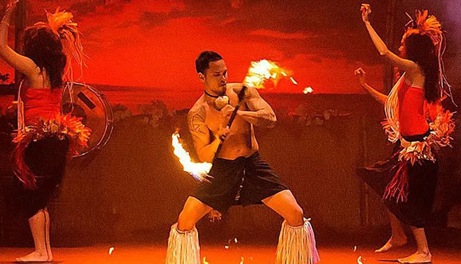 Performers engage in a dynamic fire dance, exhibiting cultural tradition and skill against a vivid, red backdrop.