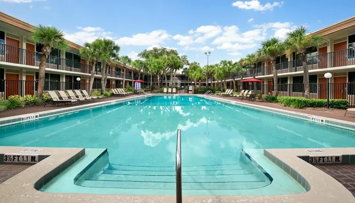 A symmetrical image of a tranquil hotel pool area flanked by two-storied buildings with palm trees under a clear blue sky