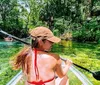 A person is kayaking in clear verdant waters surrounded by lush greenery on a sunny day