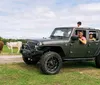 A family enjoys a drive in a black Jeep Wrangler with cows in the background in a countrified setting