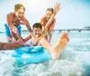 A group of joyful people is having fun in the sea with a young person on an inflatable ring taking in the sun near a pier