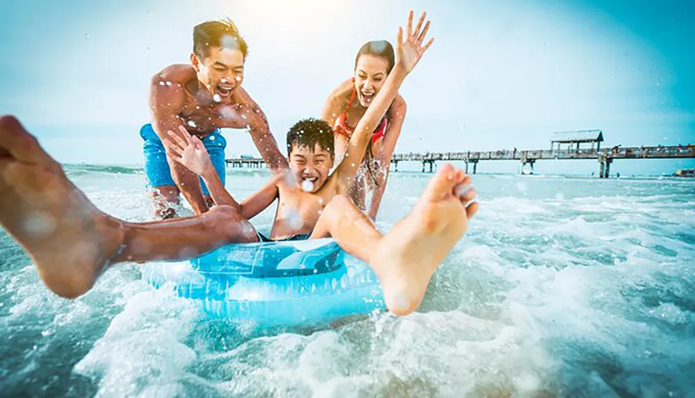 A group of joyful people is having fun in the sea with a young person on an inflatable ring taking in the sun near a pier