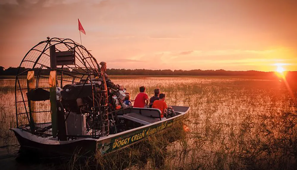 An airboat glides through a waterway at sunset carrying passengers who are likely enjoying a scenic tour