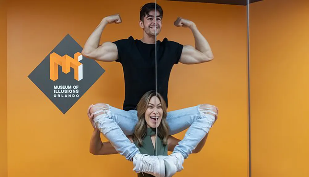 The image shows a man flexing his muscles with a woman appearing to be hanging from his biceps creating a playful illusion at the Museum of Illusions Orlando