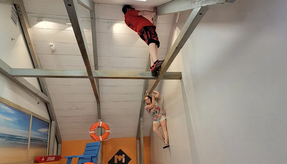 The image shows an optical illusion with two people seemingly defying gravity a person in red shorts climbing a ladder on the ceiling and another person hanging from a ledge on the wall
