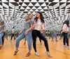 Two women are laughing and posing for a photo in a mirrored room that creates an infinite reflection effect