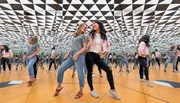 Two women are laughing and posing for a photo in a mirrored room that creates an infinite reflection effect.
