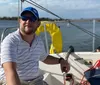 Three people are enjoying a sunny day sailing on a white sailboat with the coastline in the background