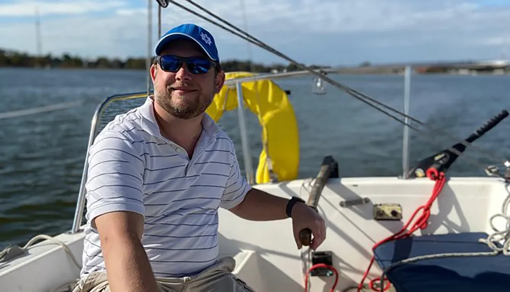 A smiling person is steering a sailboat on a sunny day