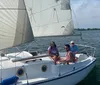 Three people are enjoying a sunny day sailing on a white sailboat with the coastline in the background