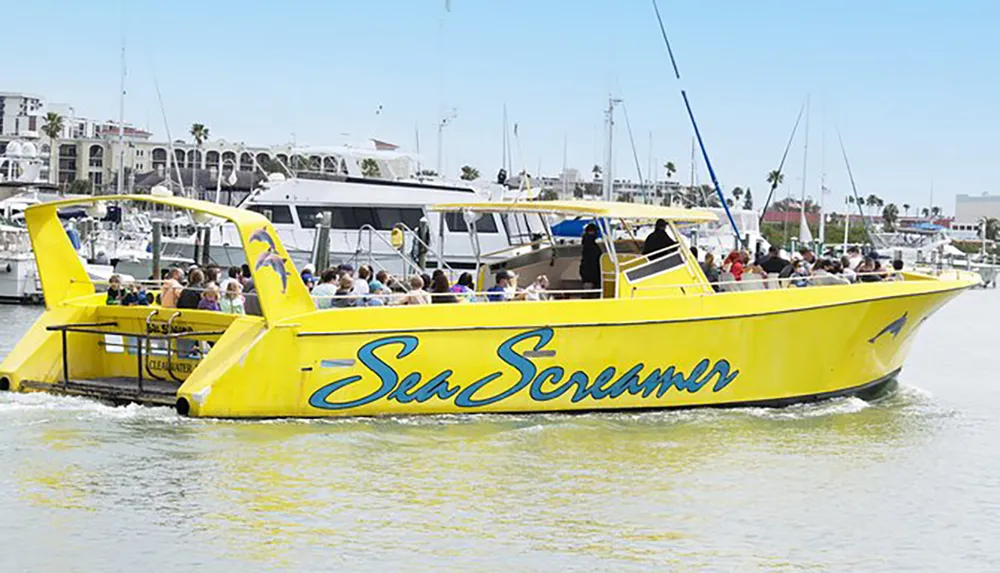 A large group of passengers enjoys a ride on a bright yellow speedboat named Sea Screamer in a sunny harbor setting