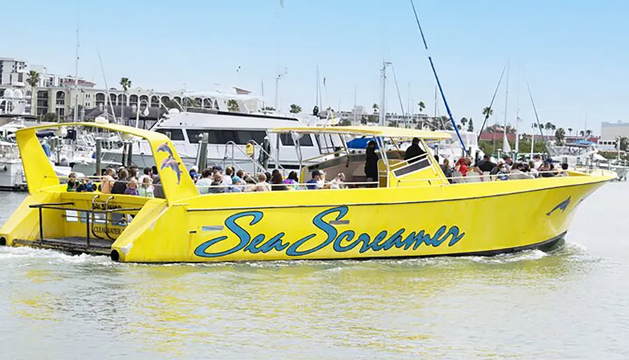 A large group of passengers enjoys a ride on a bright yellow speedboat named Sea Screamer in a sunny harbor setting.