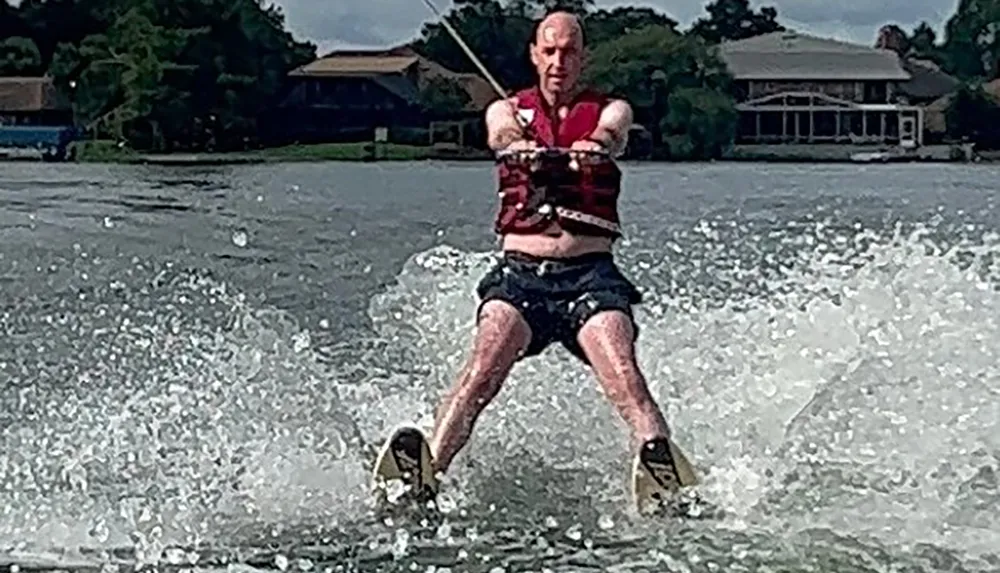 A person is water skiing on a lake clad in a life vest and shorts with an expression of concentration on their face