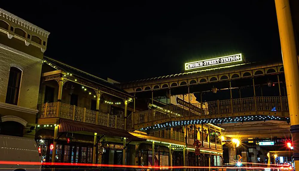 The image captures the illuminated signage of Church Street Station on a vintage-style building at night highlighted by streaks of light from passing traffic