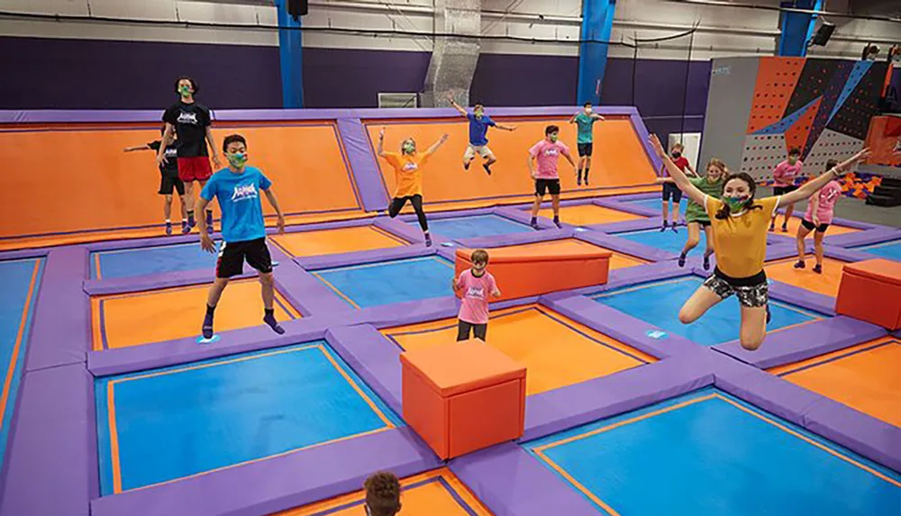 The image shows a group of people of various ages enjoying themselves by jumping and playing on a colorful indoor trampoline park