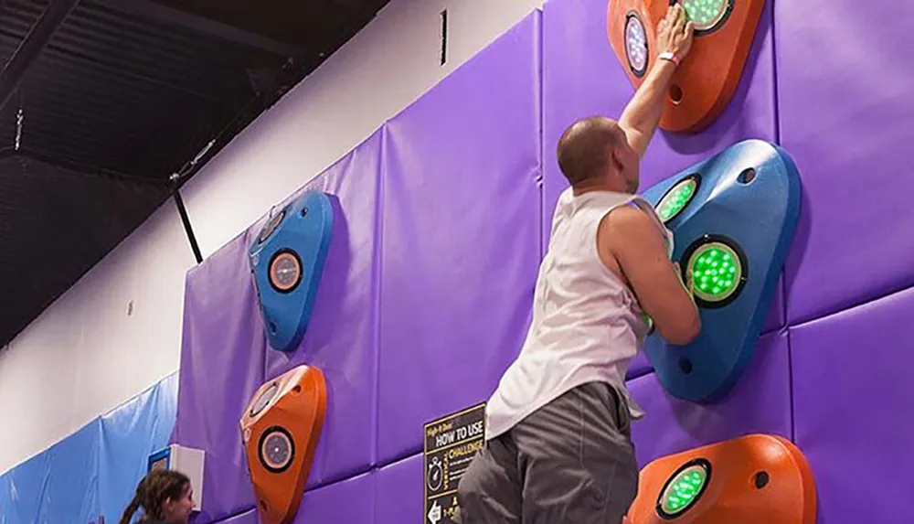 A person is engaged in an indoor climbing activity using colorful holds with integrated lights possibly for a game or training purposes