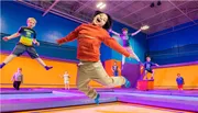 Children are joyfully jumping and playing on colorful trampolines in an indoor trampoline park.