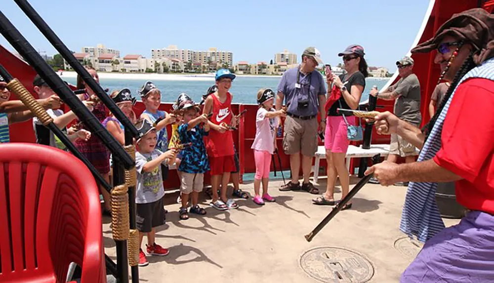 A group of children and adults some wearing pirate hats are enjoying an interactive pirate-themed boat experience on a sunny day