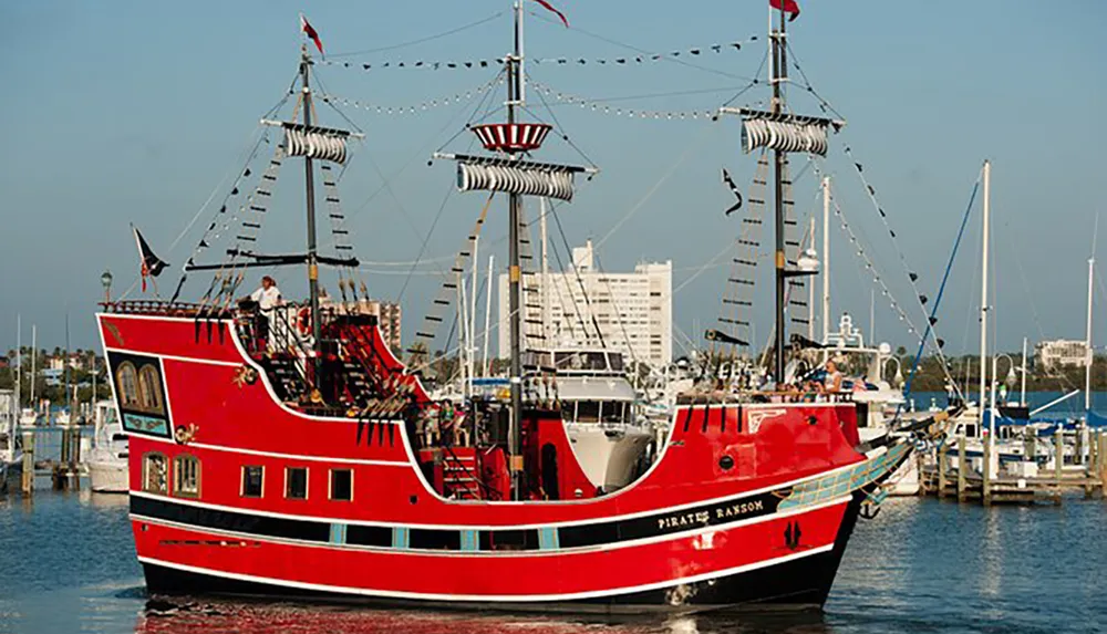 A red boat designed to look like a pirate ship named Pirates Ransom is docked in a marina with a clear sky in the background