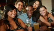 A group of five smiling friends enjoying drinks together at a social gathering.