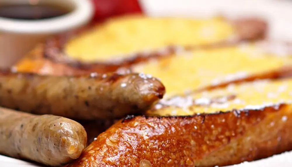 The image shows a plate with two golden brown slices of French toast and a pair of grilled sausages typically served as a breakfast meal