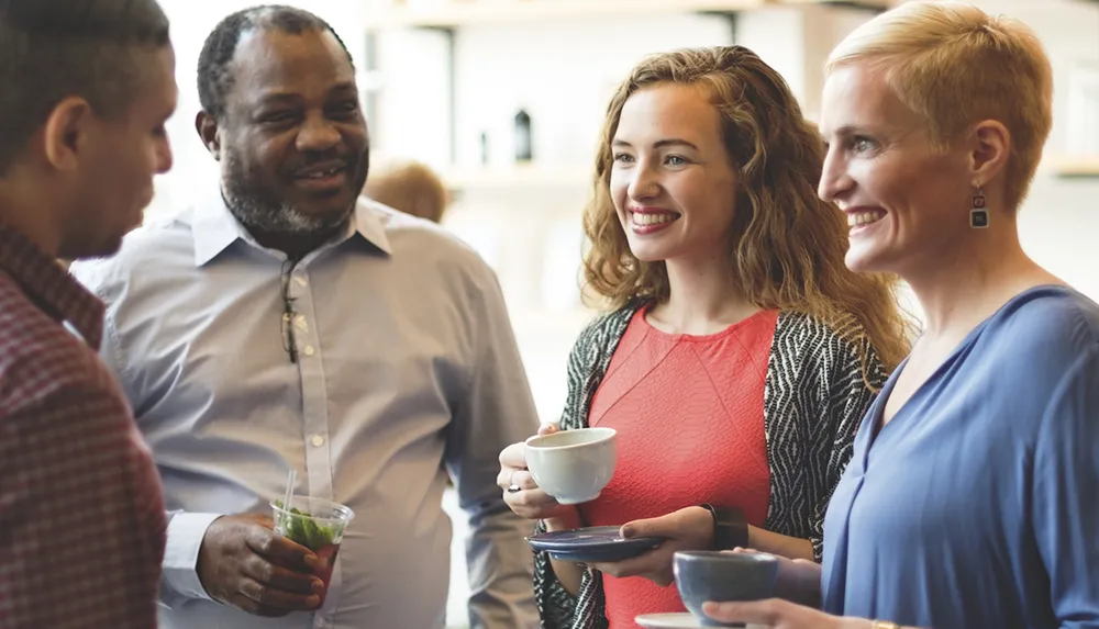 A group of four adults is engaging in a pleasant conversation while holding drinks during what appears to be a casual social gathering