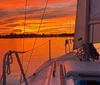 A sailboat glides on the water against a beautiful sunset backdrop with the suns rays creating a striking silhouette of the sails