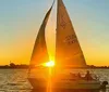 A sailboat glides on the water against a beautiful sunset backdrop with the suns rays creating a striking silhouette of the sails