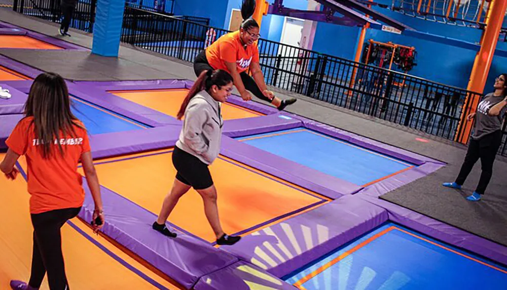 People are enjoying themselves at an indoor trampoline park with colorful trampolines and padding