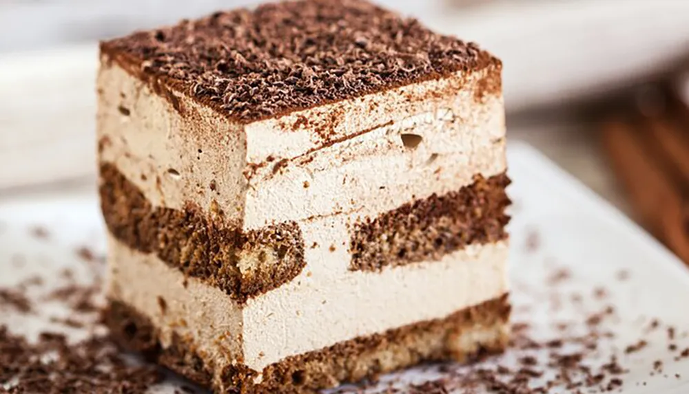 The image showcases a slice of tiramisu a classic Italian dessert with distinct layers of coffee-soaked sponge and mascarpone cream topped with a dusting of cocoa or chocolate shavings