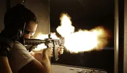 A person is firing a rifle, causing a bright muzzle flash in a dimly lit environment.