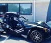 A person is driving a three-wheeled Polaris Slingshot on a bridge with a city skyline in the background