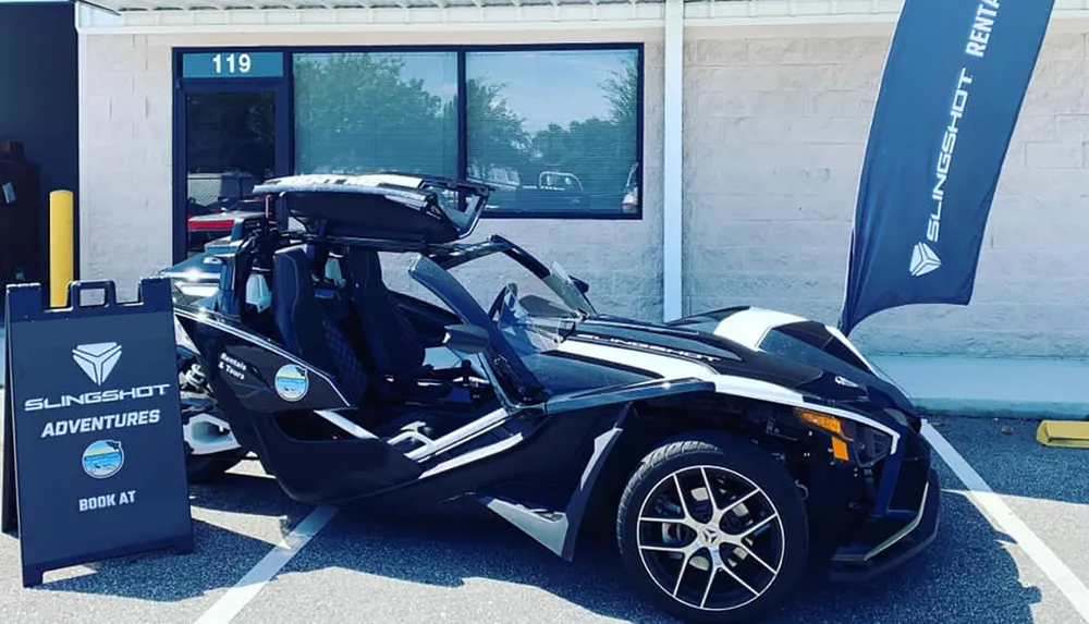 The image shows a Polaris Slingshot a three-wheeled motor vehicle parked outside a storefront advertising Slingshot rentals under clear skies