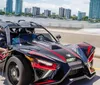 A person is driving a three-wheeled Polaris Slingshot on a bridge with a city skyline in the background