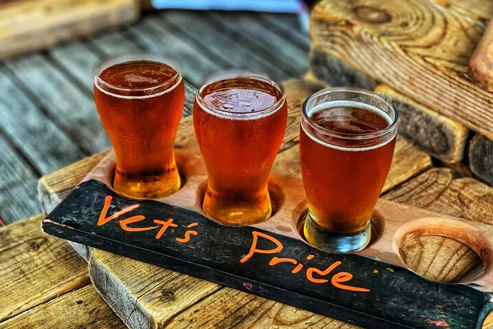 Three glasses of beer are presented on a wooden board labeled Vets Pride possibly indicating a themed beer tasting or a toast to veterans