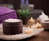 A person is smiling seated next to a massage table in a tranquil room decorated with inspirational wall art and soft lighting