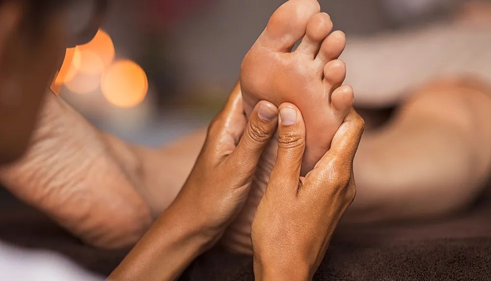 A person is giving another person a foot massage in a calming setting with soft lighting