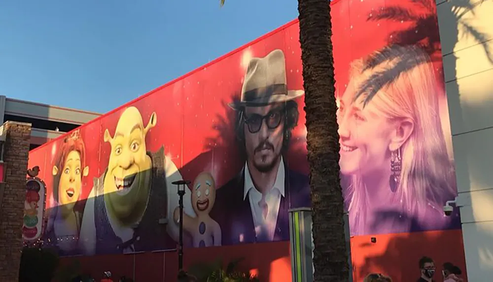 A mural on a building features a collage of animated characters and actors including Shrek and characters from Gingerbread Man with a man and a womans face portrayed realistically amongst them